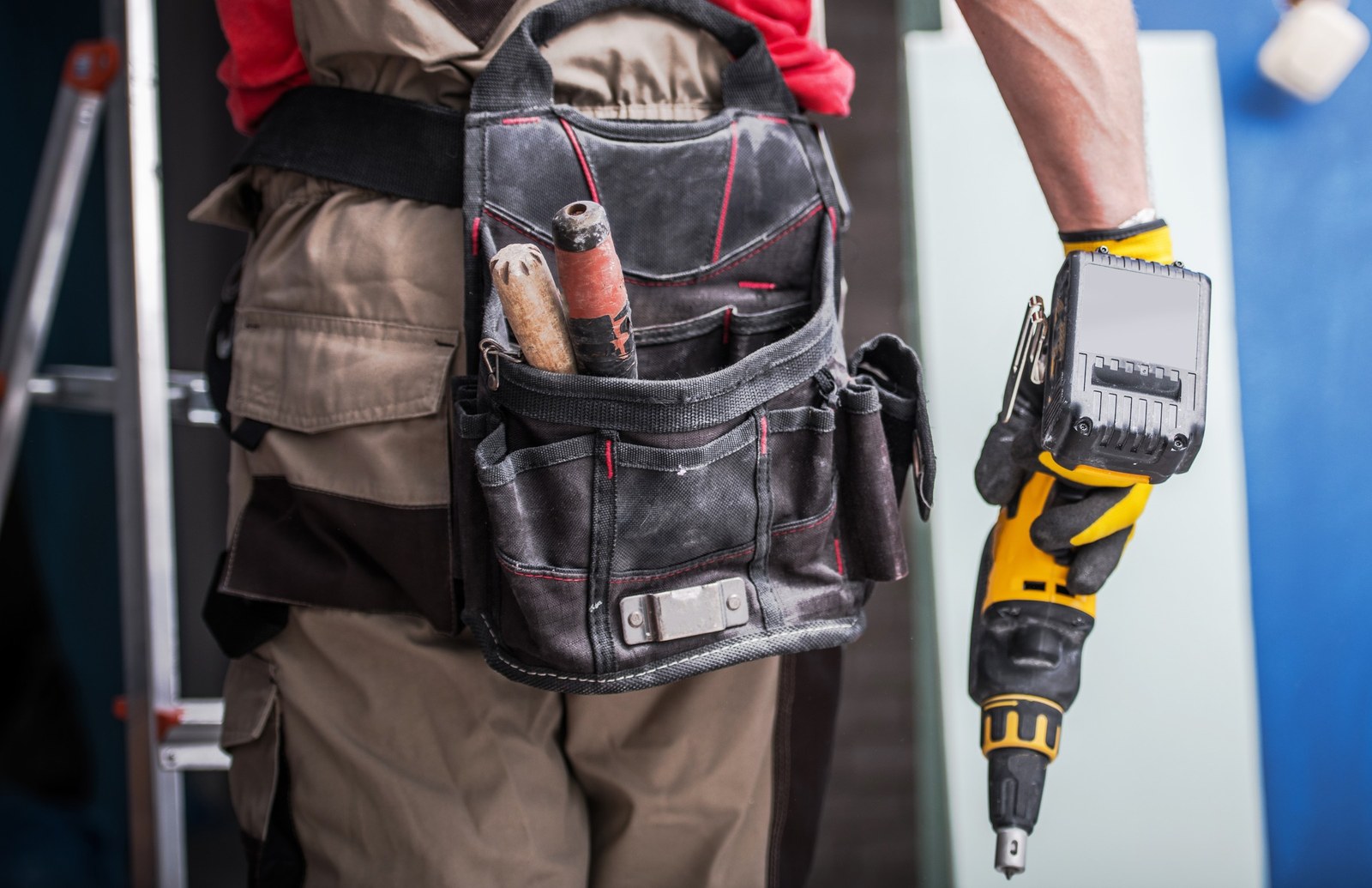 Worker in a red shirt wearing a tool belt and holding a cordless drill